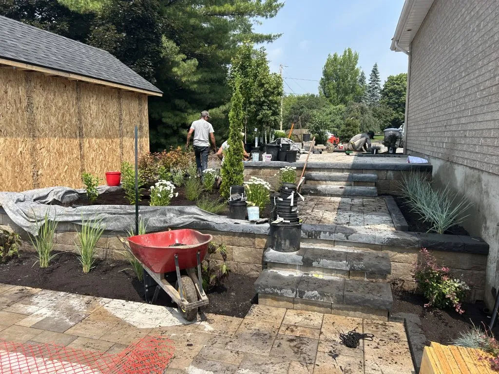 Aménagement paysager en cours avec installation de pavé uni, escalier en pierre et plantation sur terrain résidentiel après excavation et nivellement travaux extérieurs